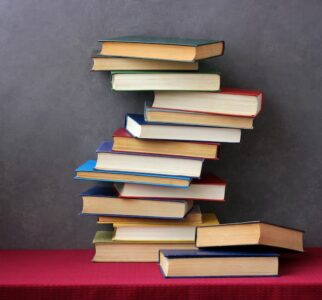 A stack of hardcover books balanced on a red surface against a grey background.